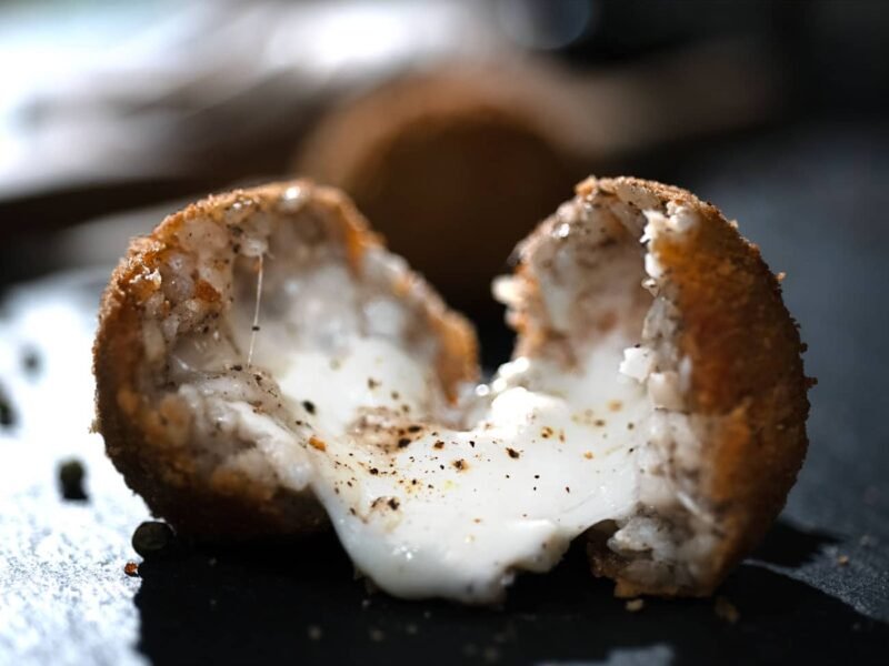 Arancino al tartufo aperto a metà su un tavolo di ardesia. Il ripieno visibile è ricolmo di mozzarella fusa