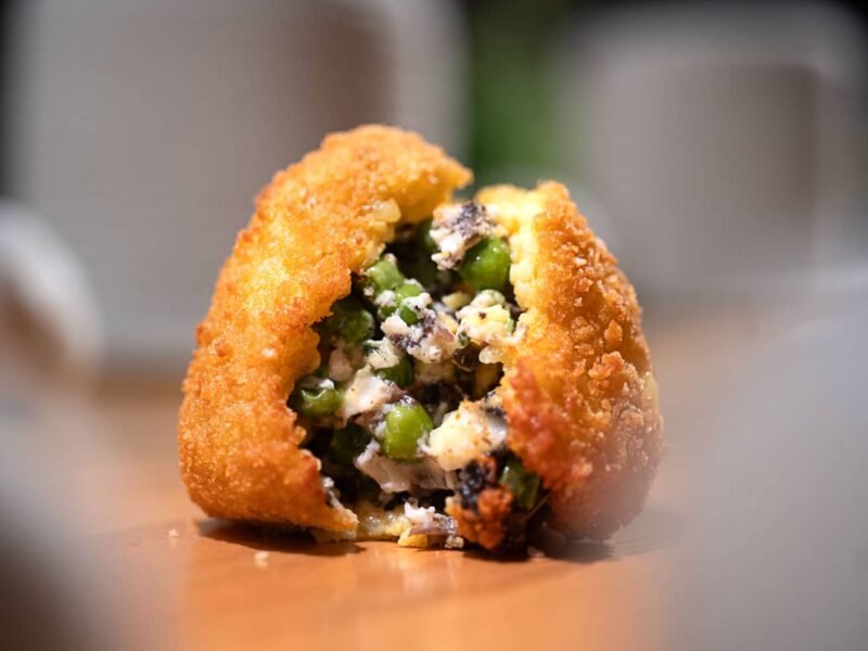 Arancino Bianco poggiato su un tavolo di legno, aperto a metà con il ripieno dei funghi e dei piselli ben visibile
