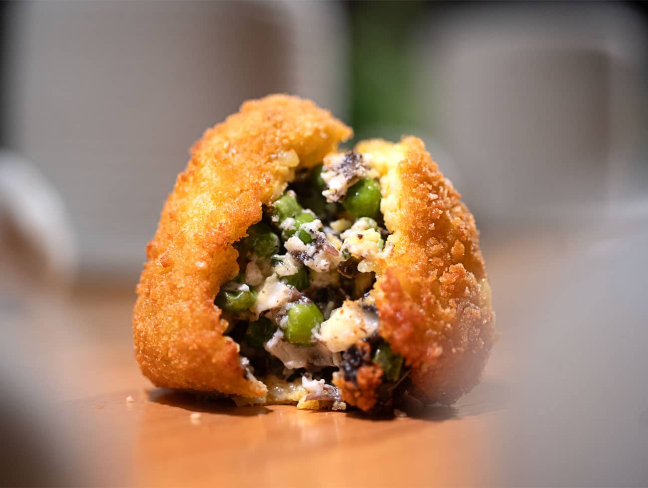 Arancino Bianco poggiato su un tavolo di legno, aperto a metà con il ripieno dei funghi e dei piselli ben visibile
