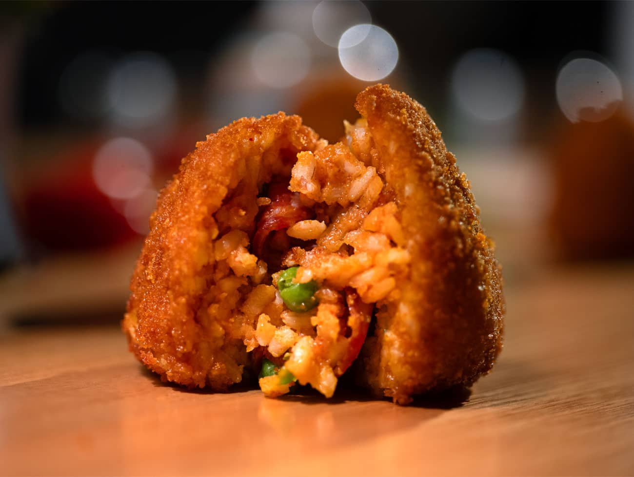 Arancino piccante poggiato su un tavolo e aperto. Si possono vedere i pezzi di salame piccante e i piselli.