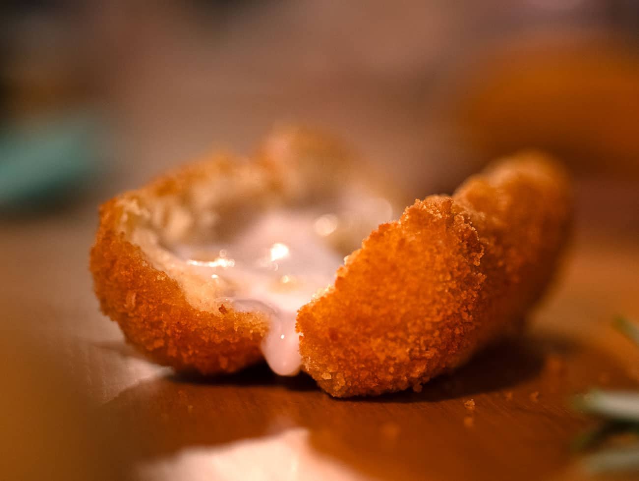 Foto di una crocchetta di. patate tagliata a metà con il ripieno di patate e mozzarella fusa ben visibile poggiato su un tavolo di legno