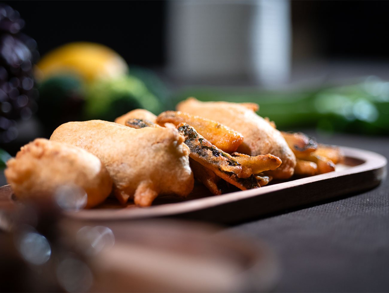 Foto di un piattino ovale di legno con poggiate sopra i pastellati (le verdure fritte)