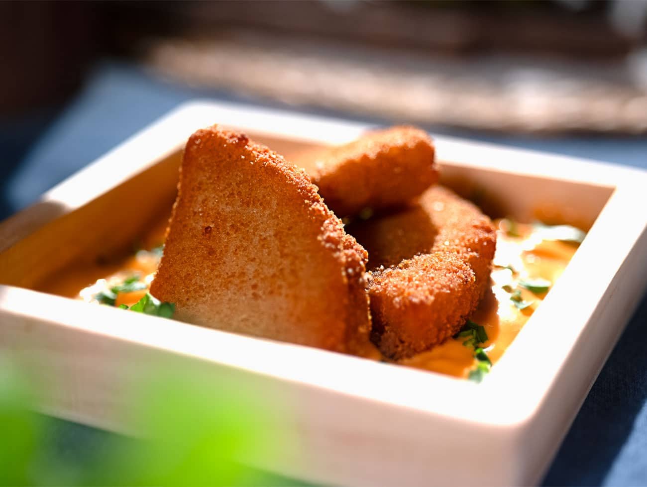 Foto di nuggy (bocconcini) di pollo poggiati su un letto di salsa e inseriti in un piattino bianco quadrato con angoli arrotondati.