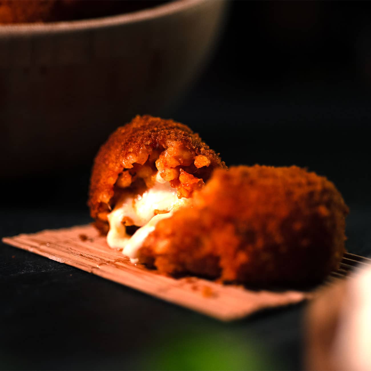 Foto di un dettaglio del supplì con carne poggiato su una piccola stuoietta poggiata a sua volta su un tavolo in ardesia.