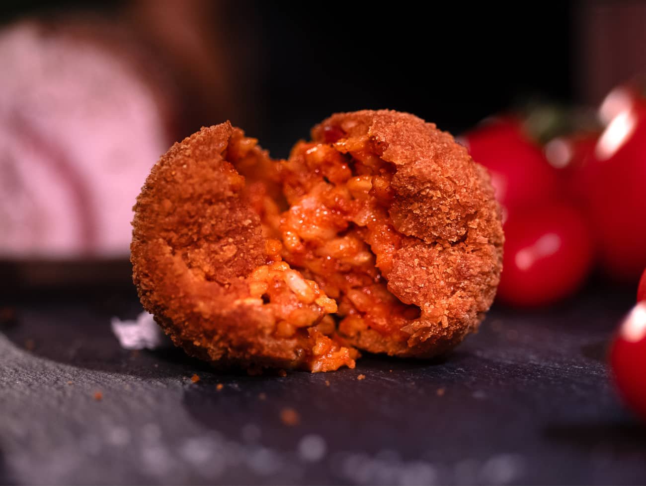 Immagine del supplì alla amatriciana aperto in due poggiato su un tavolo in ardesia