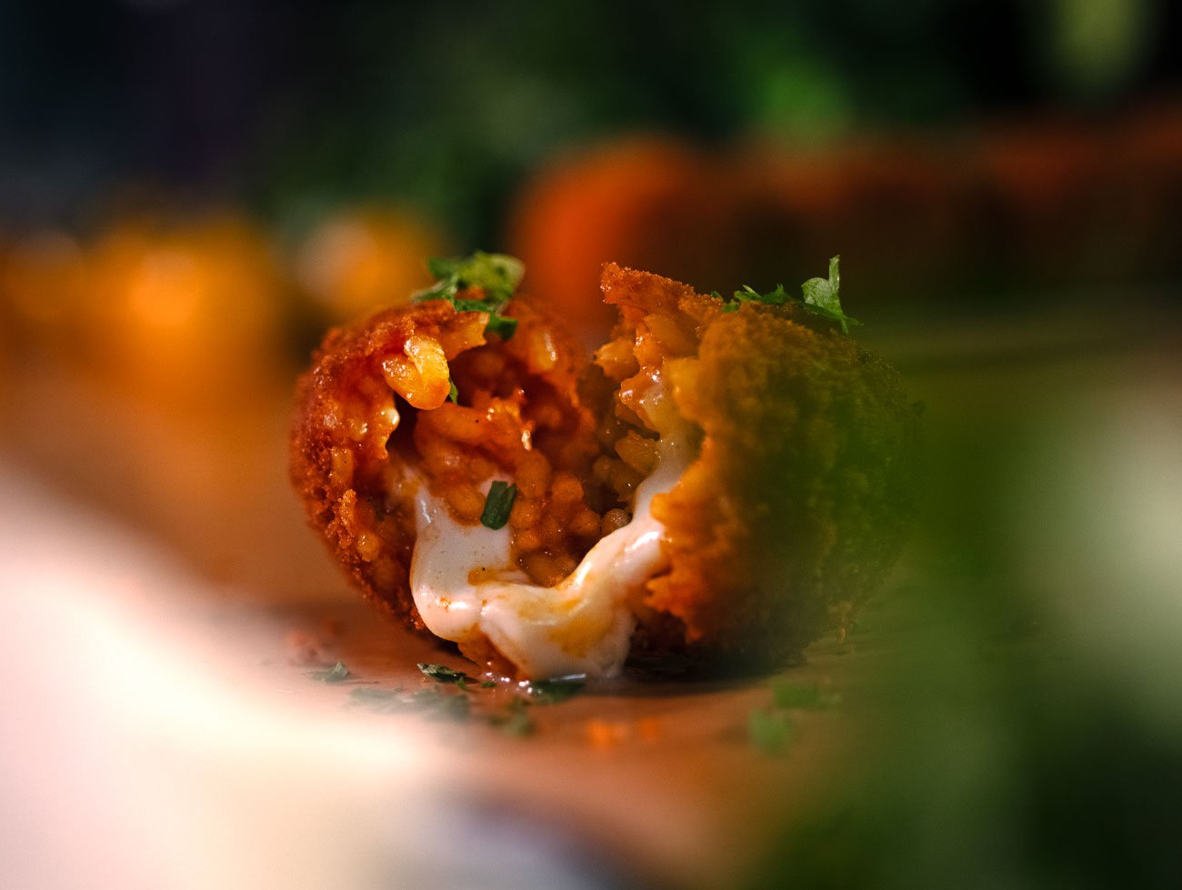 Supplì aperto a metà con la mozzarella filante che esce, presenti piccole foglie di prezzemolo come decorazione