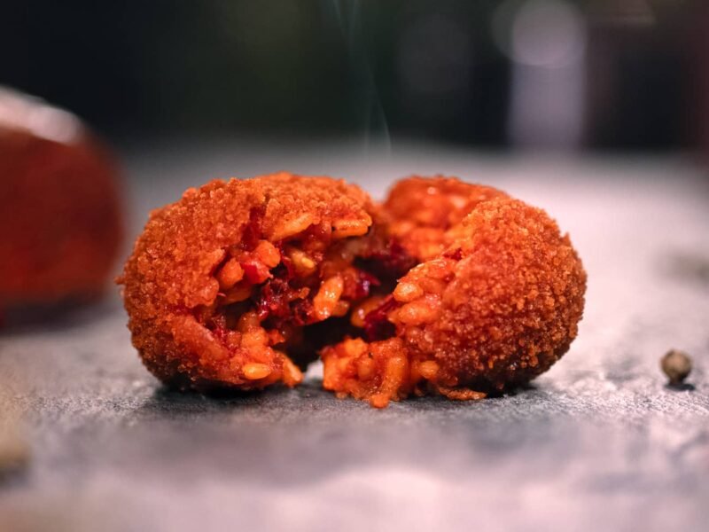 Supplì alla Nduja poggiato su un tavolo, aperto a metà e con pezzi di 'nduja visibili