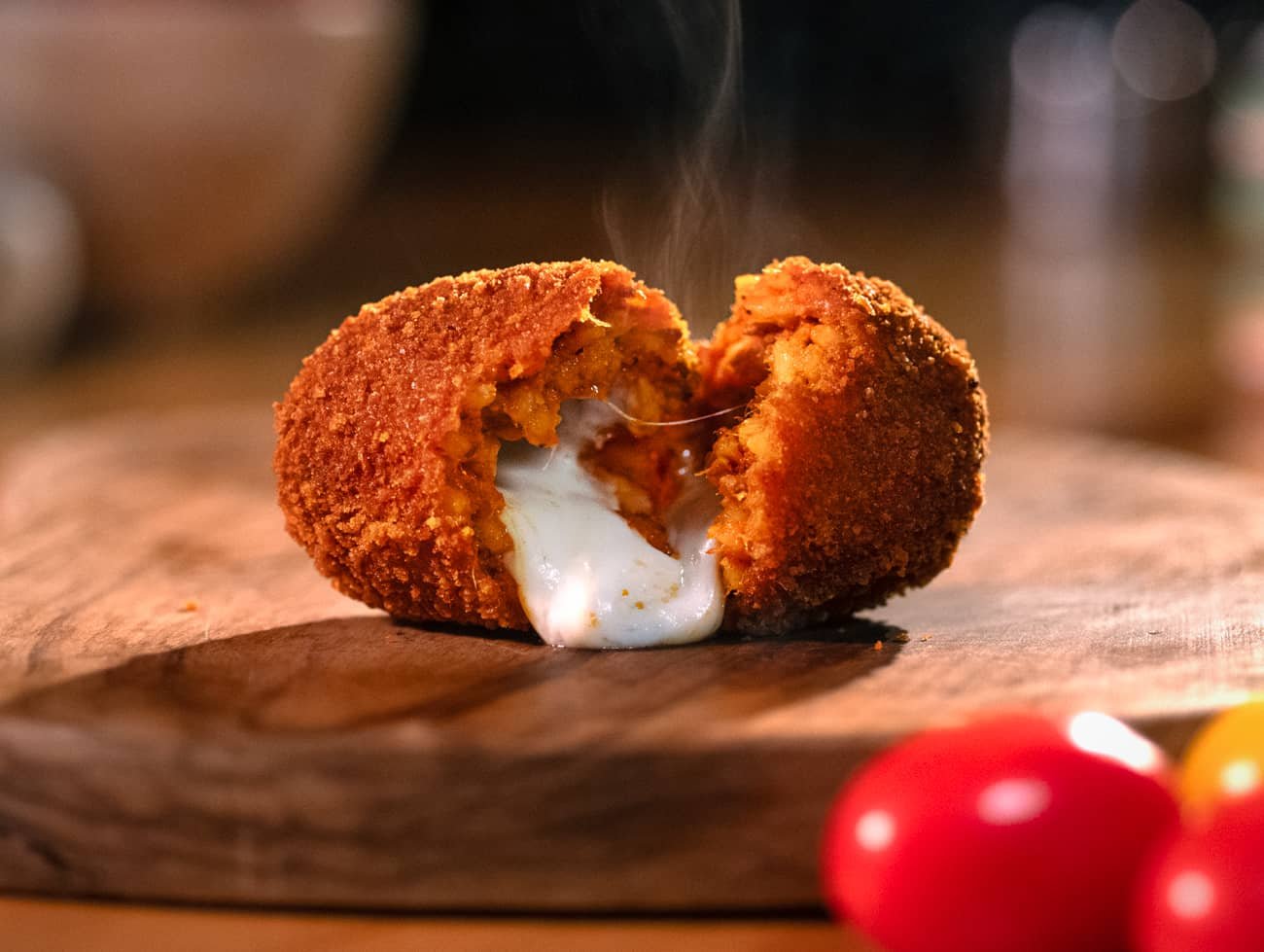 immagine del supplì della nonna poggiato su un tagliere, aperto e con la mozzarella fusa che esce e il fumo che esce